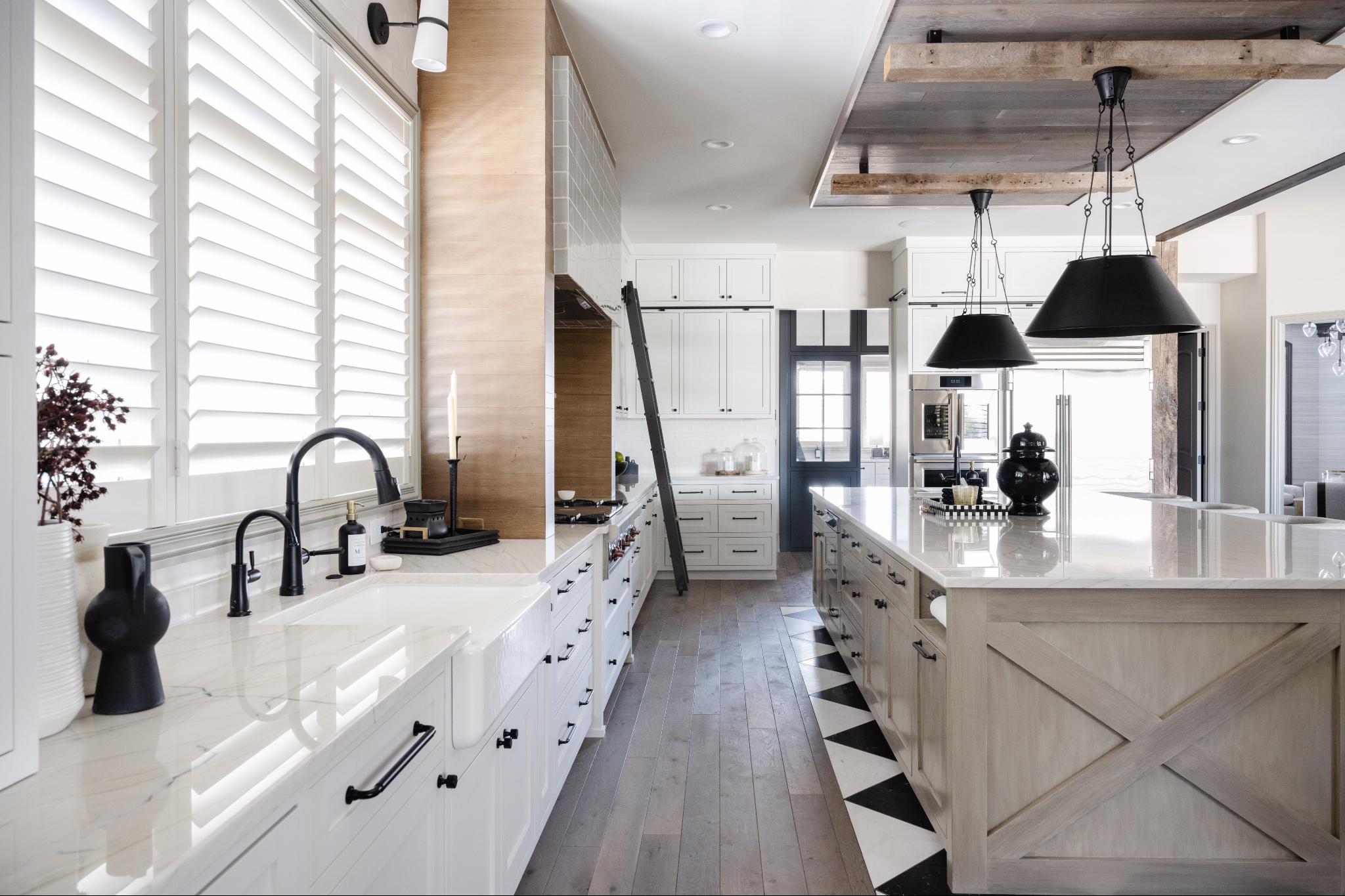 Custom kitchen designed by an interior design firm Omaha homeowners trust, featuring white cabinetry, large quartz island, wood ceiling beams, black pendant lighting, and a functional layout for everyday living.