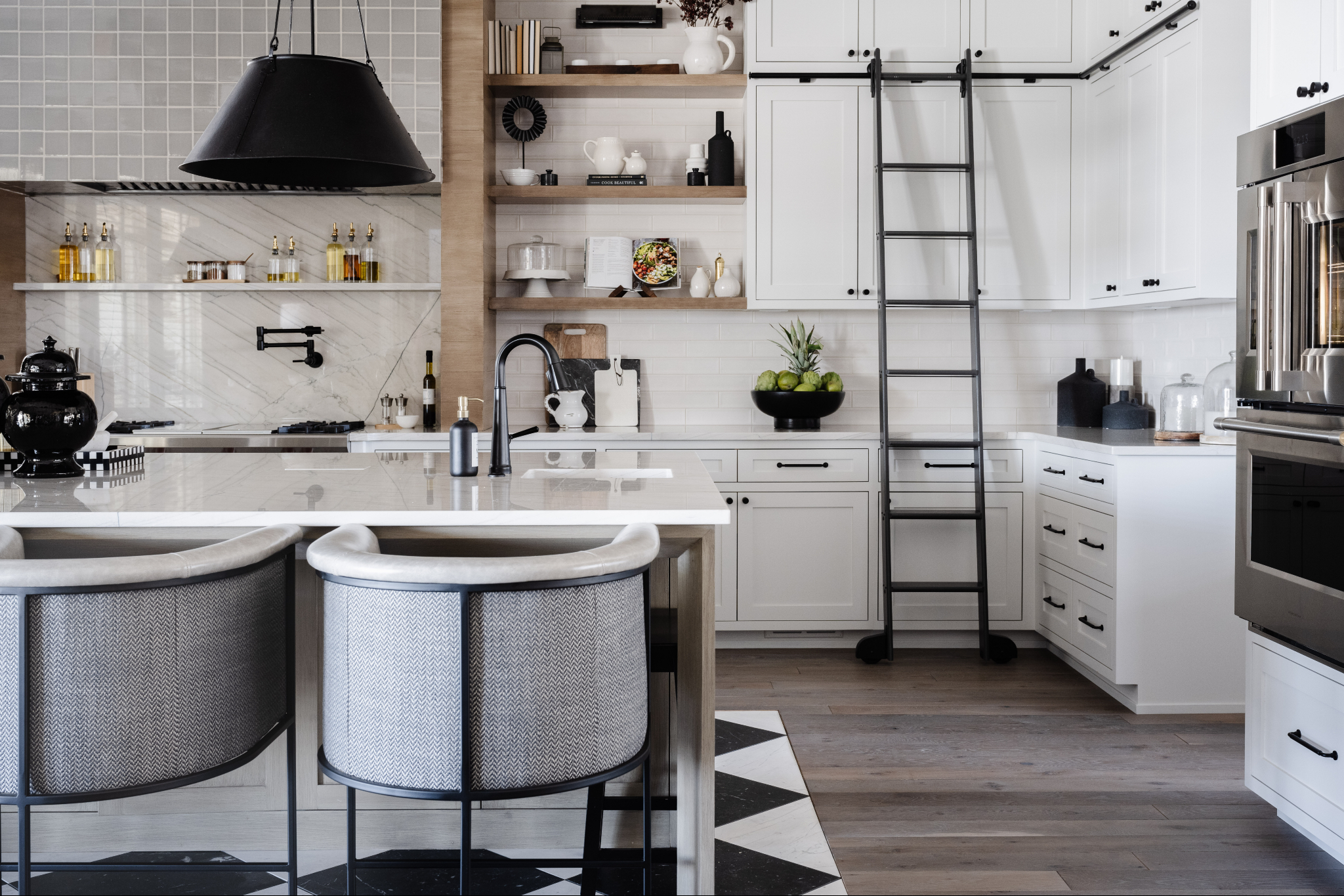 Modern kitchen showcasing Omaha interior design with custom white cabinetry, open shelving, marble backsplash, oversized black range hood, and a functional island designed for everyday living and timeless style.